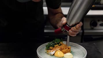 A person in a cap pouring sauce from a metal container onto a plate with food.