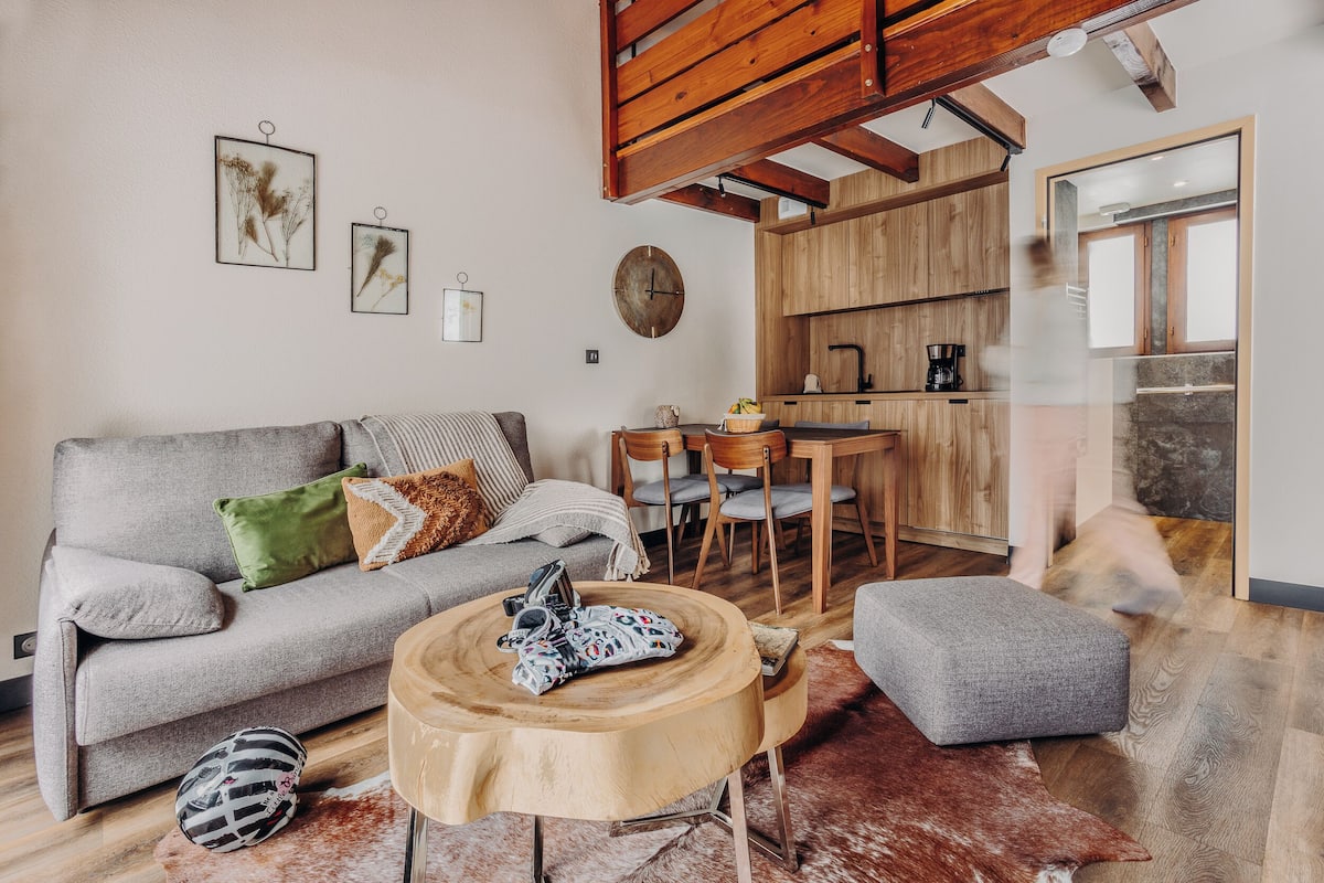 A cozy living room with a grey sofa, a round wooden coffee table, and a rustic rug.