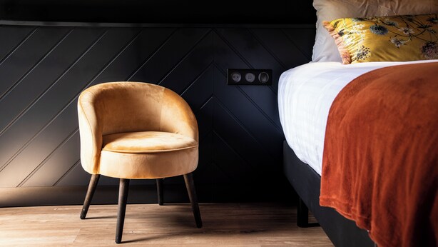 Ein moderner Raum mit einem Bett, einem Sessel und einer Wand mit geometrischem Muster.