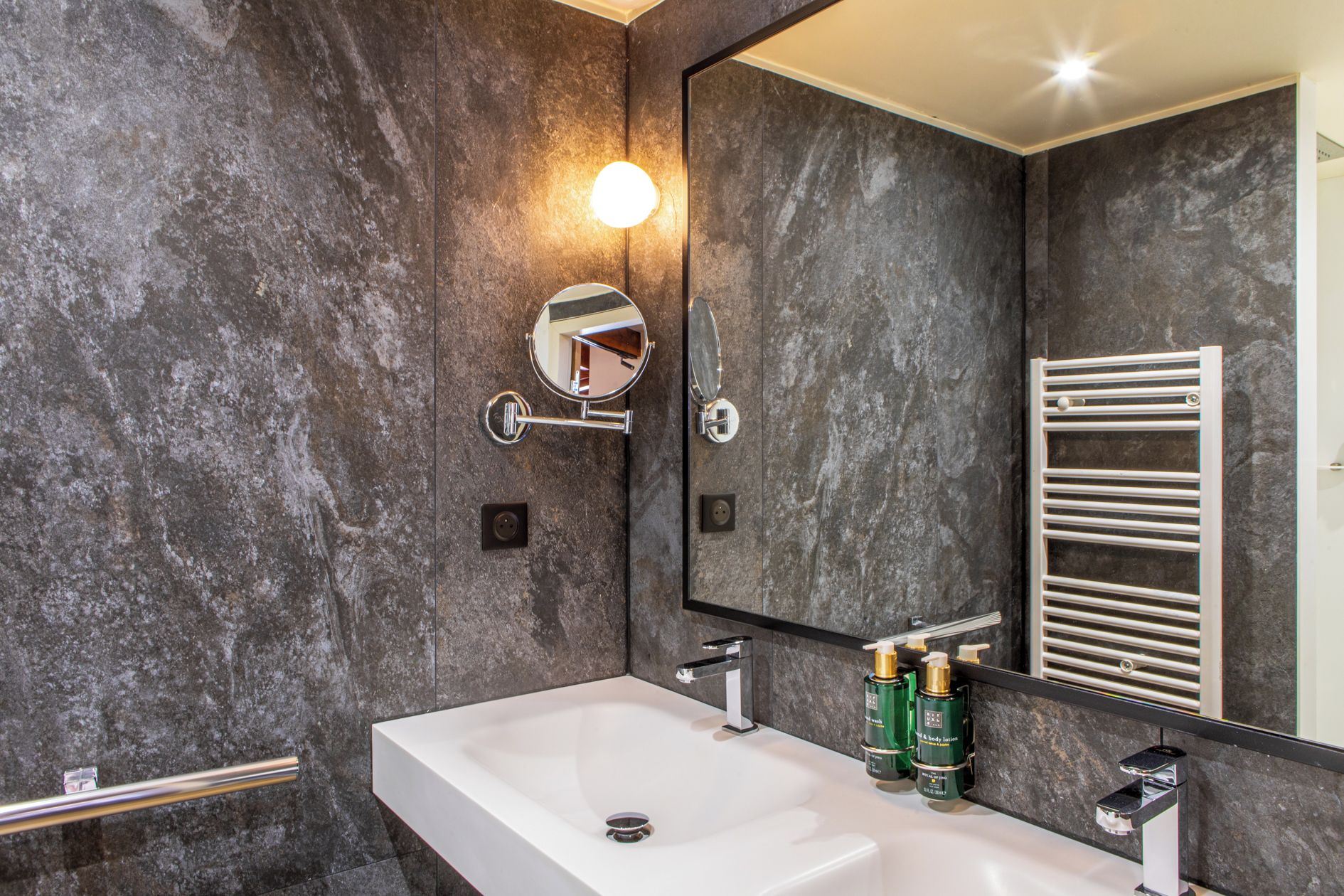 Une salle de bain moderne avec un grand miroir, un lavabo blanc et un porte-serviettes.