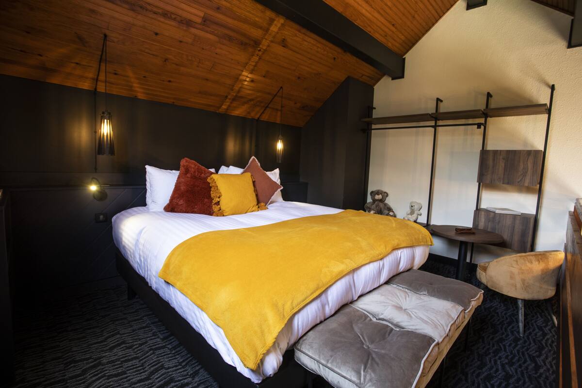 A bedroom with a bed, a bench, a table, and a chair.