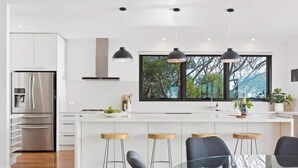 A modern kitchen with a large island, bar stools, and a stainless steel refrigerator. - The Ocean's Edge, Luxury Entertainer with Views (Mount Martha)