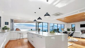 A modern kitchen with a large island, pendant lighting, and a view of the sky. - The Ocean's Edge, Luxury Entertainer with Views (Mount Martha)