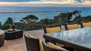 An outdoor seating area with wicker furniture and a glass table, overlooking the sea. - The Ocean's Edge, Luxury Entertainer with Views (Mount Martha)