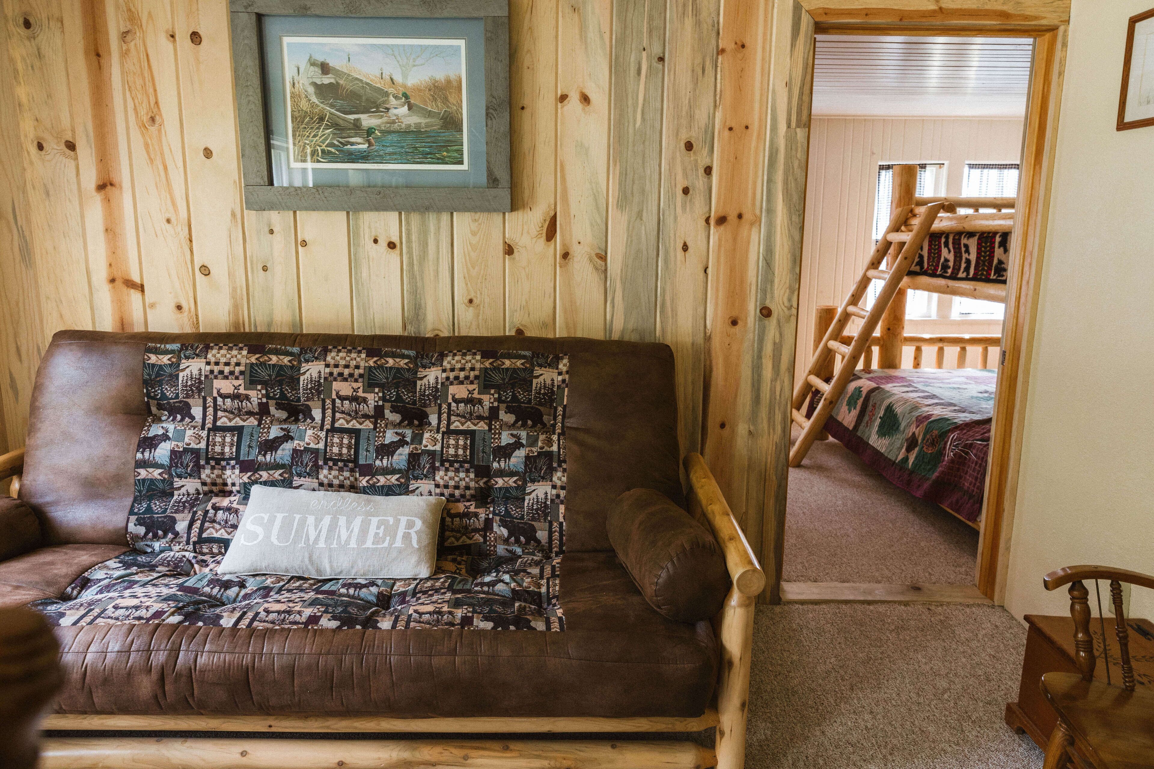 A wooden cabin interior with a sofa, a ladder, and a bunk bed.