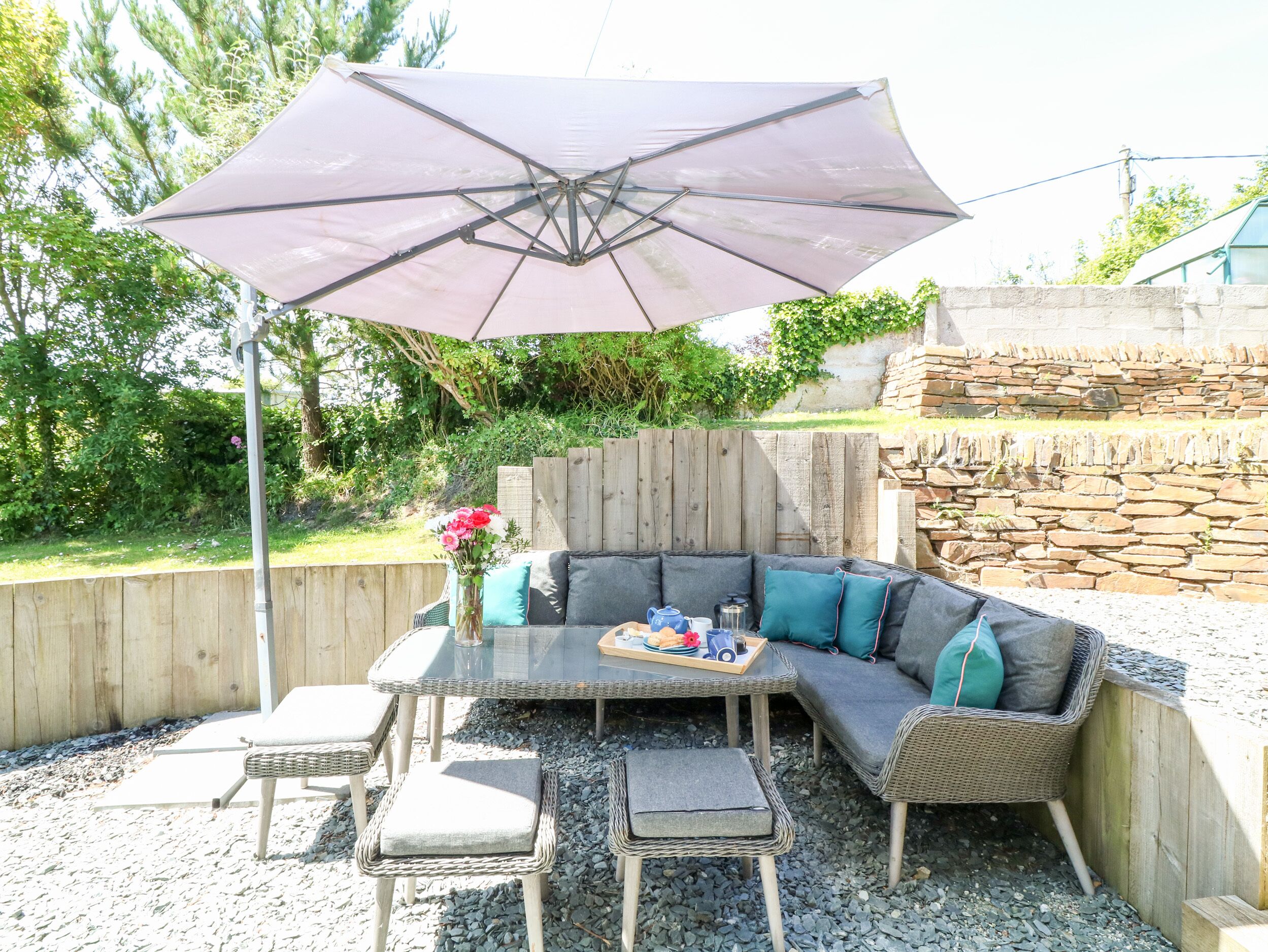 An outdoor patio with a glass-top table, wicker chairs, a cushioned sofa, and a large umbrella.