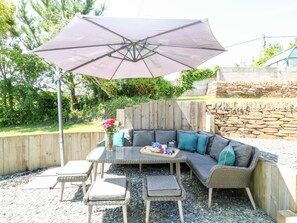 An outdoor patio with a glass-top table, wicker chairs, a cushioned sofa, and a large umbrella. - Kelmscot (Port Isaac)