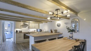 A modern kitchen with wooden beams, a central island, and a dining area with chairs. - Kelmscot (Port Isaac)
