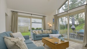 A modern living room with a blue sofa set, a wooden coffee table, and a large sliding glass door leading to an outdoor area. - Kelmscot (Port Isaac)