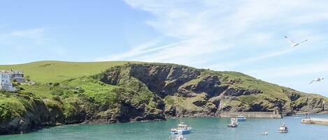 A coastal scene with boats docked near a rocky shoreline, a white building, and a clear sky.