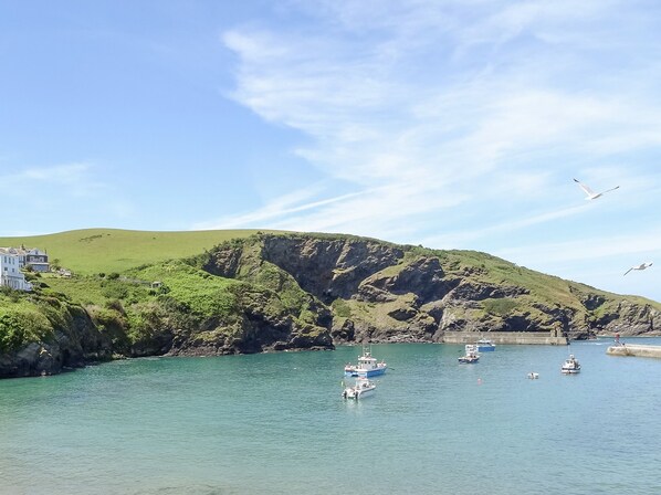 A coastal scene with boats docked near a rocky shoreline, a white building, and a clear sky.