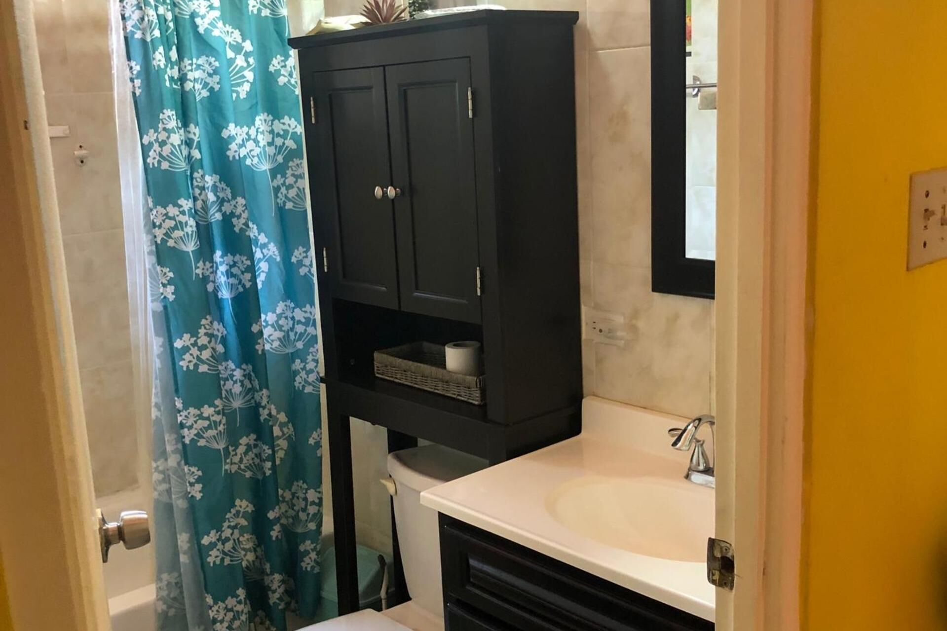 Une salle de bain avec un meuble noir, un lavabo blanc et un rideau de douche à motifs floraux bleus.
