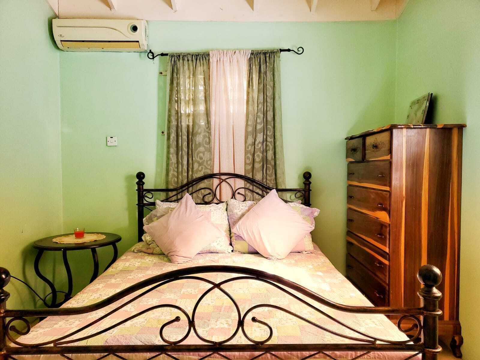 A bedroom with a bed, a dresser, a small table, and a window with curtains.