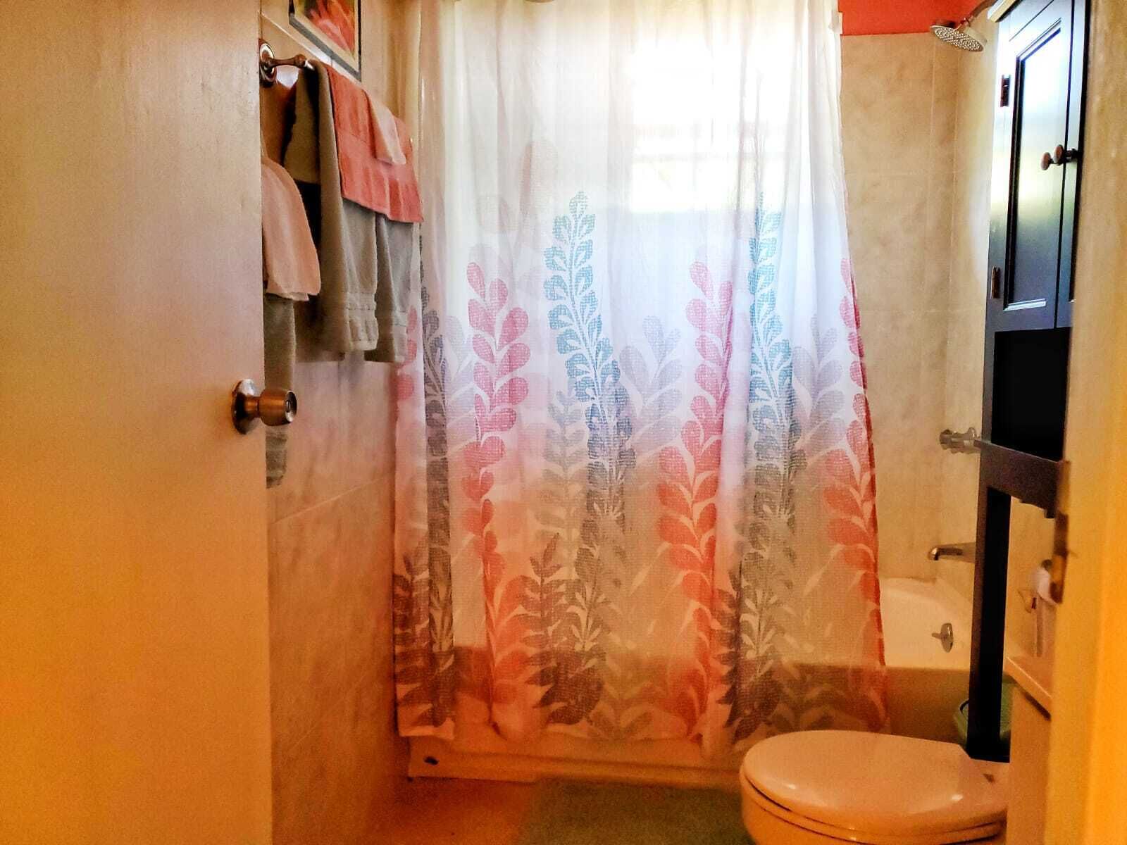 Ein Badezimmer mit Toilette, einer Duschvorhang mit Blumenmuster und einem Handtuchhalter mit Handtüchern.