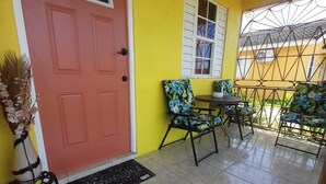A yellow building with a red door, a small patio with two chairs and a table, and a decorative plant. - 2 Bed-sleeps 4-gated Community-5 Min Town Centre (Falmouth)