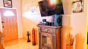 A living room with a fireplace, a television on top, and two vases with dried plants. - 2 Bed-sleeps 4-gated Community-5 Min Town Centre (Falmouth)