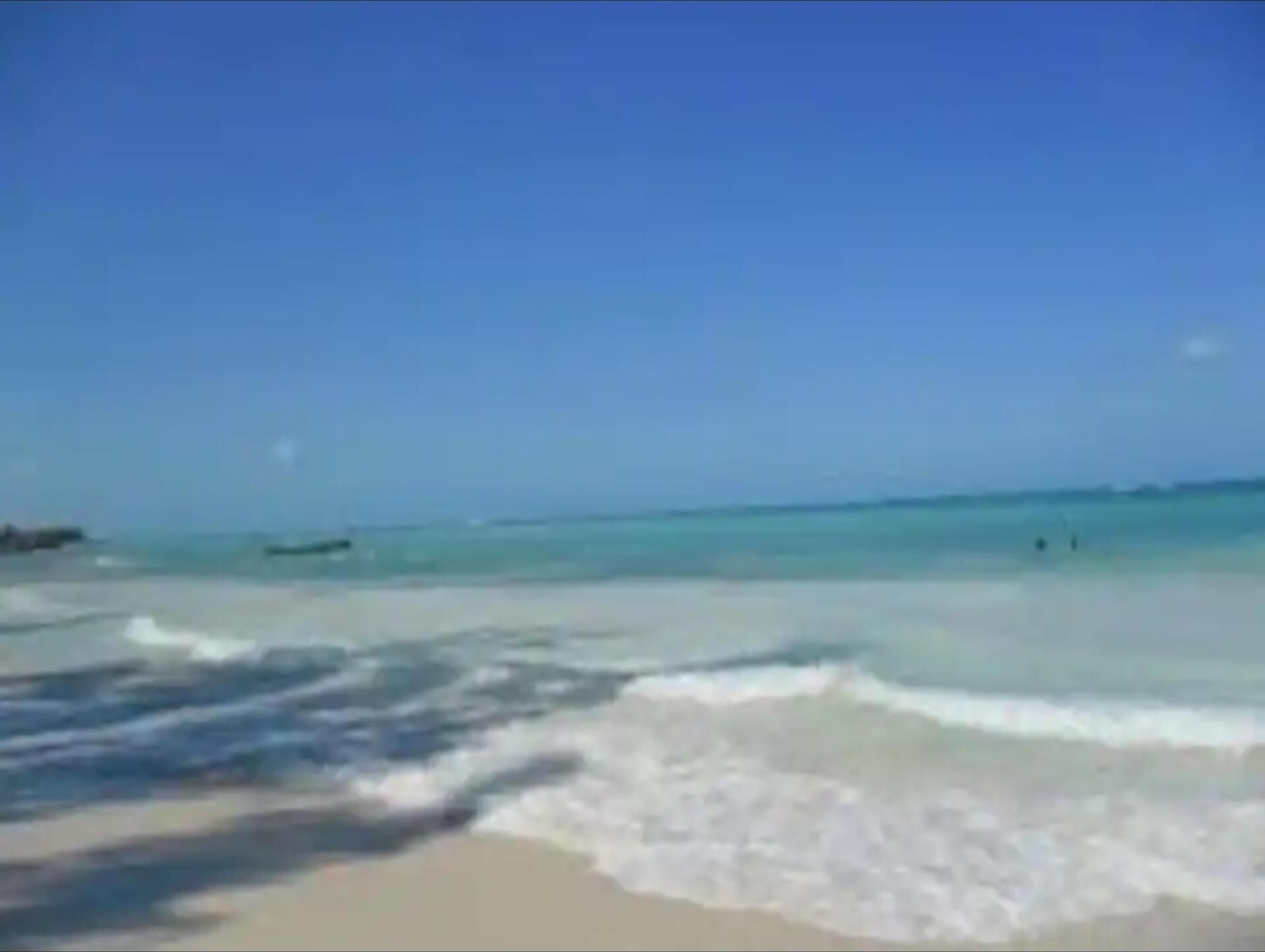 A beach with clear blue water and a sandy shore.