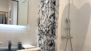 Un baño con cortina de ducha blanca y negra con motivos florales, un lavamanos moderno con un espejo encima y un cabezal de ducha.