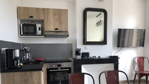 Cocina compacta con microondas, horno y cafetera. Hay una mesa de comedor con sillas y un televisor montado en la pared.