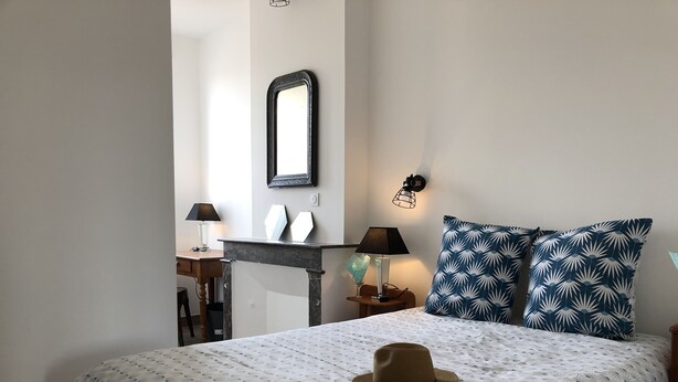 Un dormitorio con cama, mesita de noche, escritorio, silla, espejo y lámpara de pared.