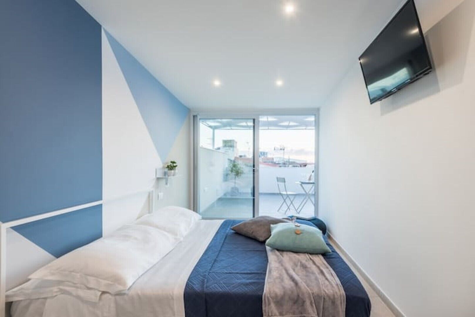 Een moderne slaapkamer met een bed, een aan de muur bevestigde televisie en een balkon met uitzicht op de stad.
