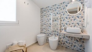 Un bagno moderno con pannelli backsplash in piastrelle geometriche, un water, un bidet e un lavabo con specchio.