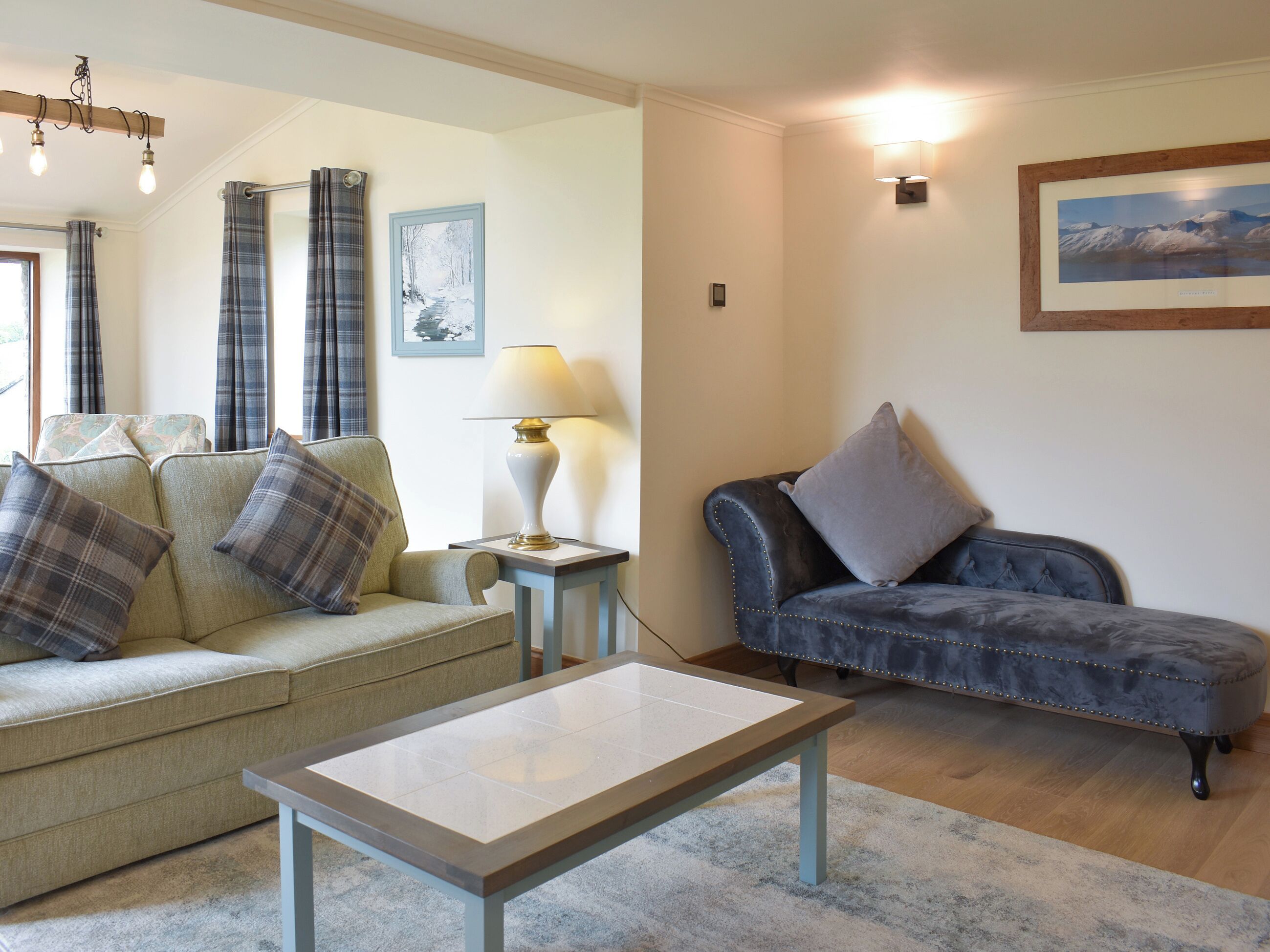 A living room with a sofa, a chaise lounge, a table, and a lamp.