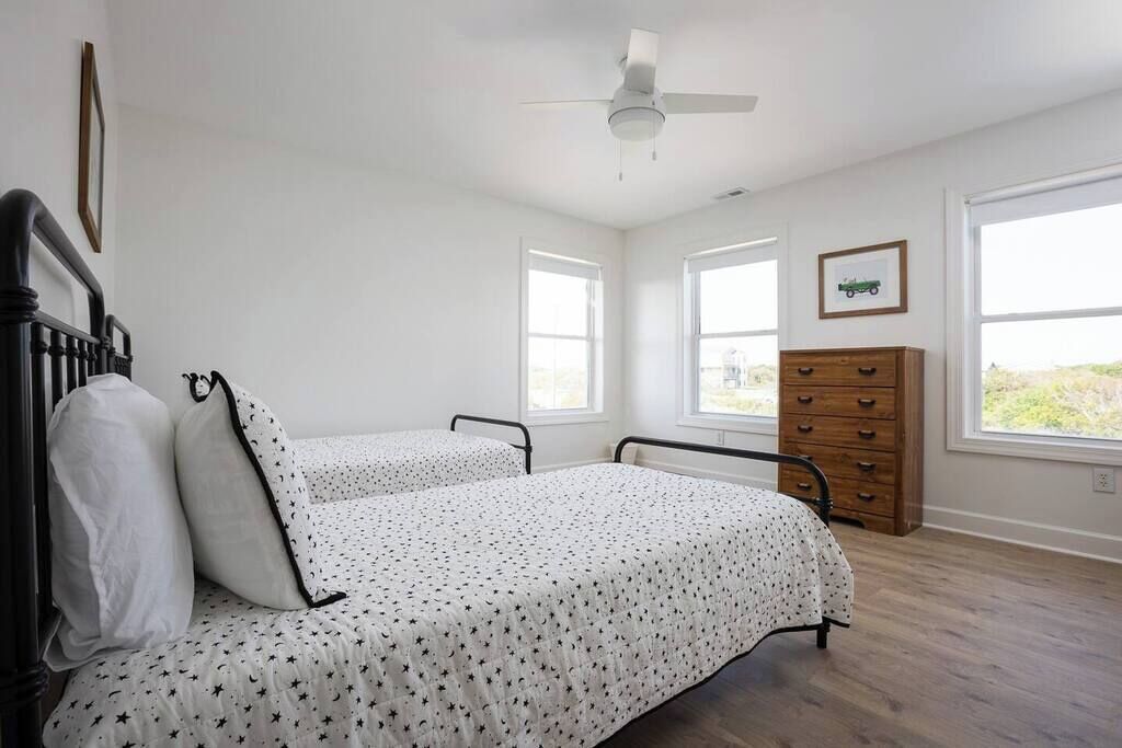A bedroom with two single beds, a ceiling fan, a dresser, and large windows.