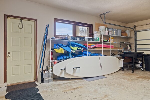 A garage with a white surfboard, a ladder, and shelves with various items.