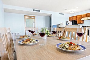 A dining table set with plates of food and wine glasses, surrounded by wooden chairs in a room with light blue walls and wooden cabinets.