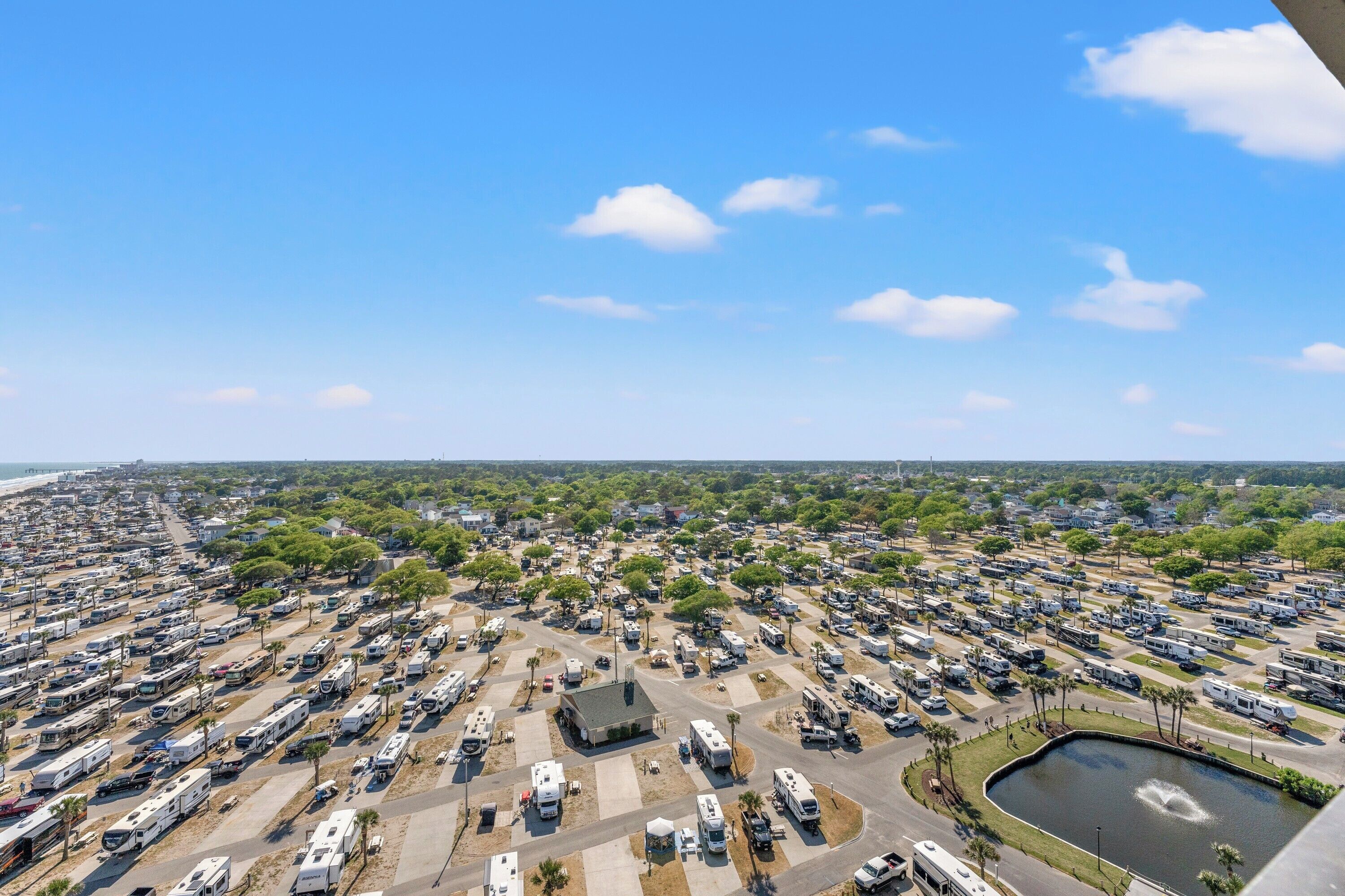A large RV park with multiple rows of RVs, a central building, and a body of water.