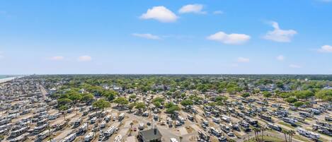 A large RV park with multiple rows of RVs, a central building, and a body of water.