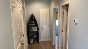 Un couloir doté d’un plancher en bois, de portes blanches et d’une petite étagère ornée d’objets décoratifs.