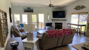 Un salon spacieux doté d’une cheminée, d’un ventilateur de plafond et d’un téléviseur fixé au mur.