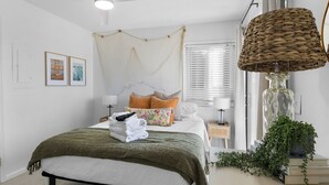Un dormitorio ordenado con cama, mesitas de noche, ventilador de techo y ventana con persianas.