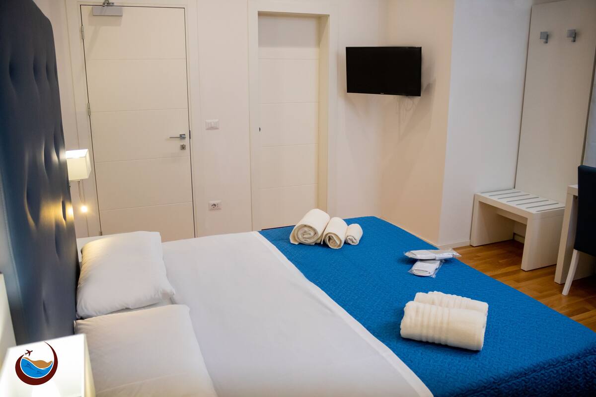 A hotel room with a bed, a TV mounted on the wall, a desk, and a chair.
