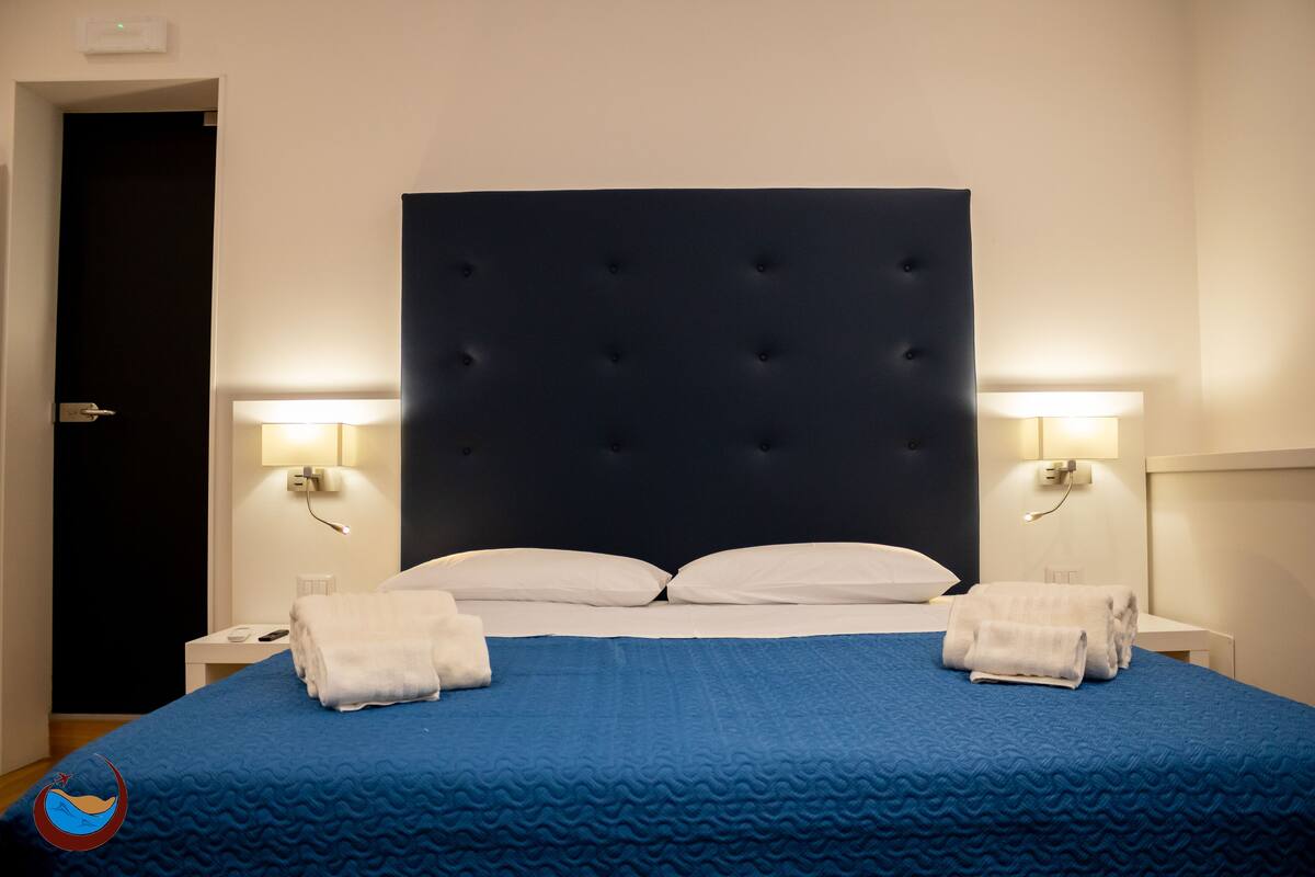 A hotel room with a large bed, two bedside tables, and wall-mounted lamps.