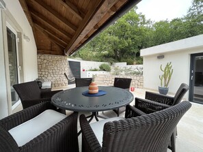 Relax in a serene outdoor space with a round table, wicker chairs, and a hanging chair, surrounded by lush greenery.