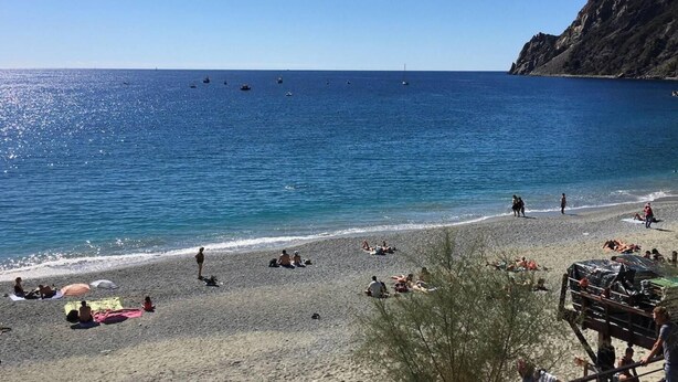 A beach with people sunbathing and swimming, a rocky cliff, and boats in the water. - Cute 1 Bedroom Apartment in La Spezia (La Spezia)