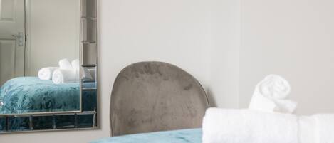 A bedroom with a bed, a headboard, a mirror, and a wall-mounted shelf.