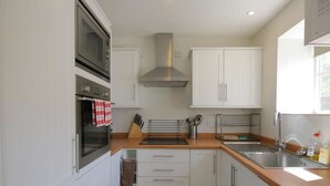 A modern kitchen with white cabinets, stainless steel appliances, and a wooden countertop. - Noel Cottage (Chipping Campden)