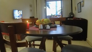 A dining area with a round table, chairs, a candle, salt and pepper shakers, and a bowl of fruit.