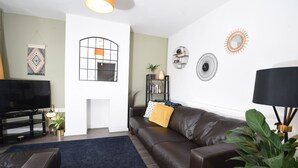 A living room with a brown leather sofa, a black TV stand, a blue rug, and a black floor lamp. - Cosy and Modern 2 Bed Family House in Abergele (Abergele)