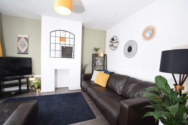 A living room with a brown leather sofa, a black TV stand, a blue rug, and a black floor lamp.