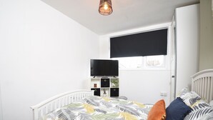 A bedroom with a bed, a TV, a window with a blind, and a white radiator. - Cosy and Modern 2 Bed Family House in Abergele (Abergele)
