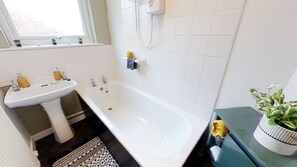 A bathroom with a white bathtub, a sink, and a window above the sink.