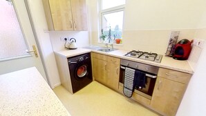 A compact kitchen with a washing machine, a sink, a stove, and wooden cabinets. - Cosy and Modern 2 Bed Family House in Abergele (Abergele)