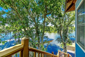 Terraza de madera con vista a un lago, árboles y un cielo azul despejado.