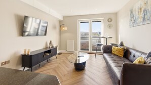 A modern living room with a glass coffee table, leather sofa, and a flat-screen TV mounted on the wall. - Properties Unique | The Peak (Newcastle Upon Tyne)