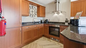 A kitchen with wooden cabinets, a stainless steel range hood, a clock, and a fire extinguisher. - Properties Unique | The Peak (Newcastle Upon Tyne)